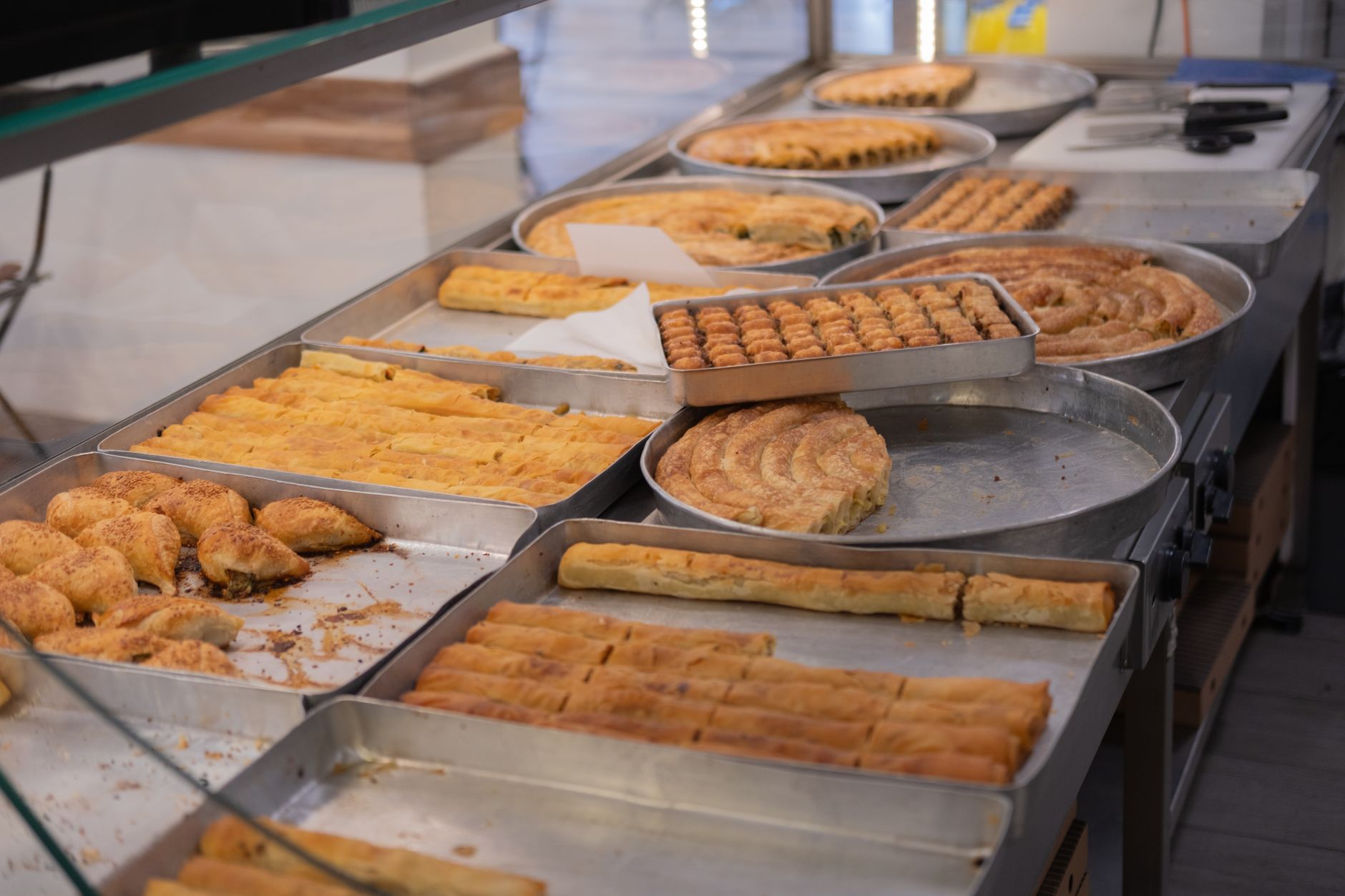Eine Auswahl an frisch gebackenen türkischen Teigwaren und Börek auf Backblechen in einer Vitrine