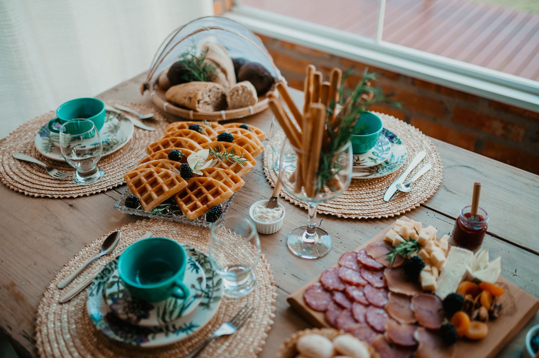 Ein rustikal gedeckter Frühstückstisch mit verschiedenen herzhaften Speisen, Waffeln und Brot auf Holzbrettern für ein gemütliches Beisammensein.