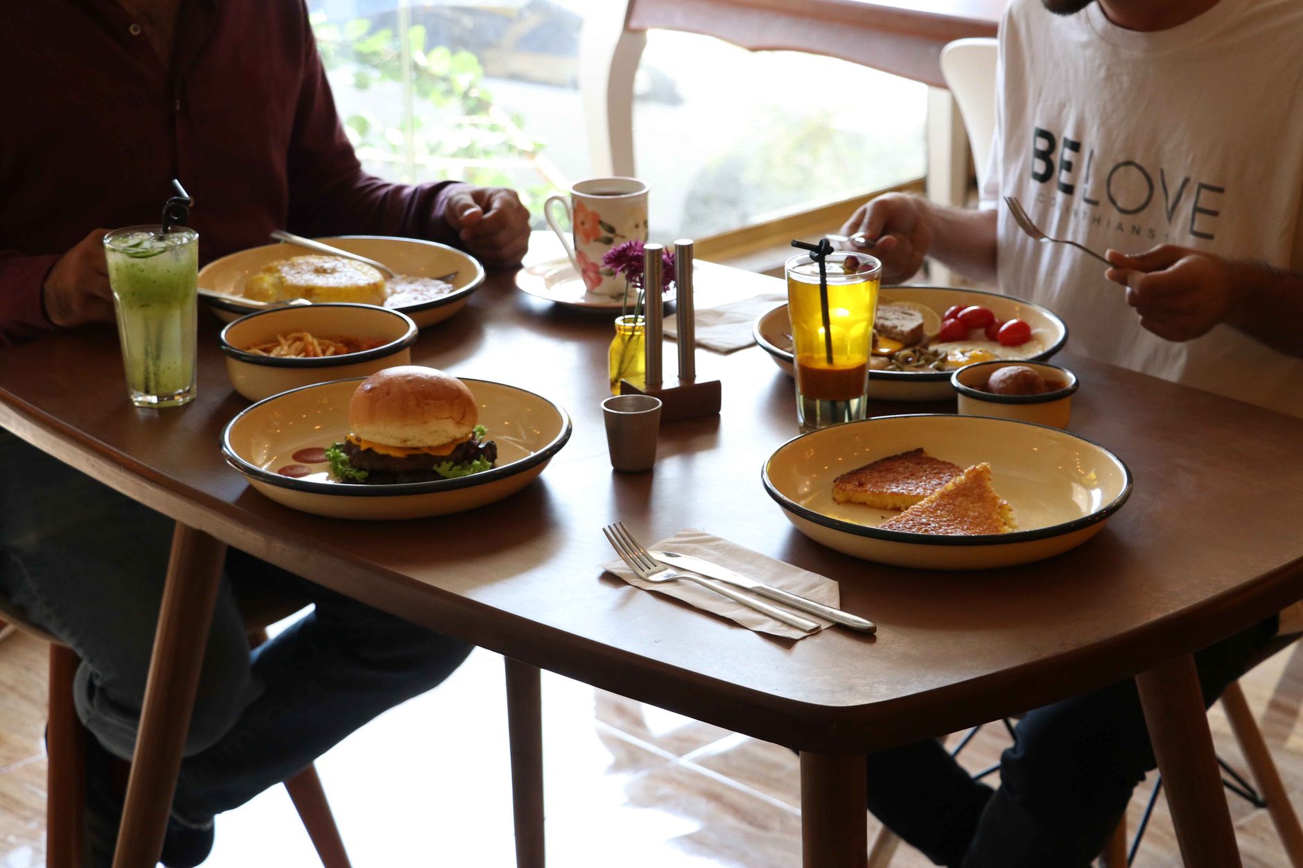 Zwei Personen sitzen entspannt an einem gedeckten Tisch im Innenraum und genießen ein gemeinsames Frühstück in gemütlicher Atmosphäre.