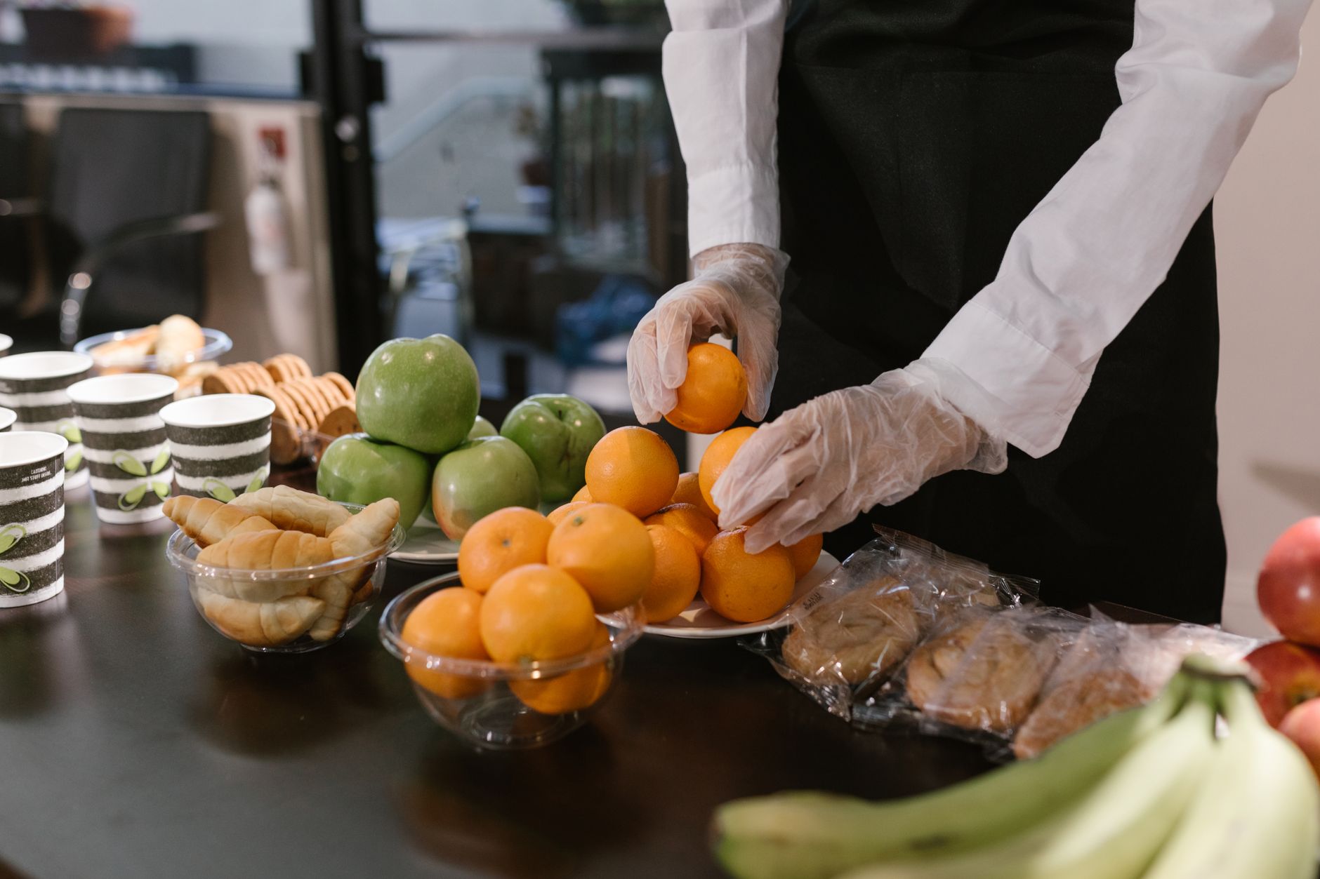 Eine Person richtet frisches Obst und Snacks auf einer reich gedeckten Catering-Tafel an.