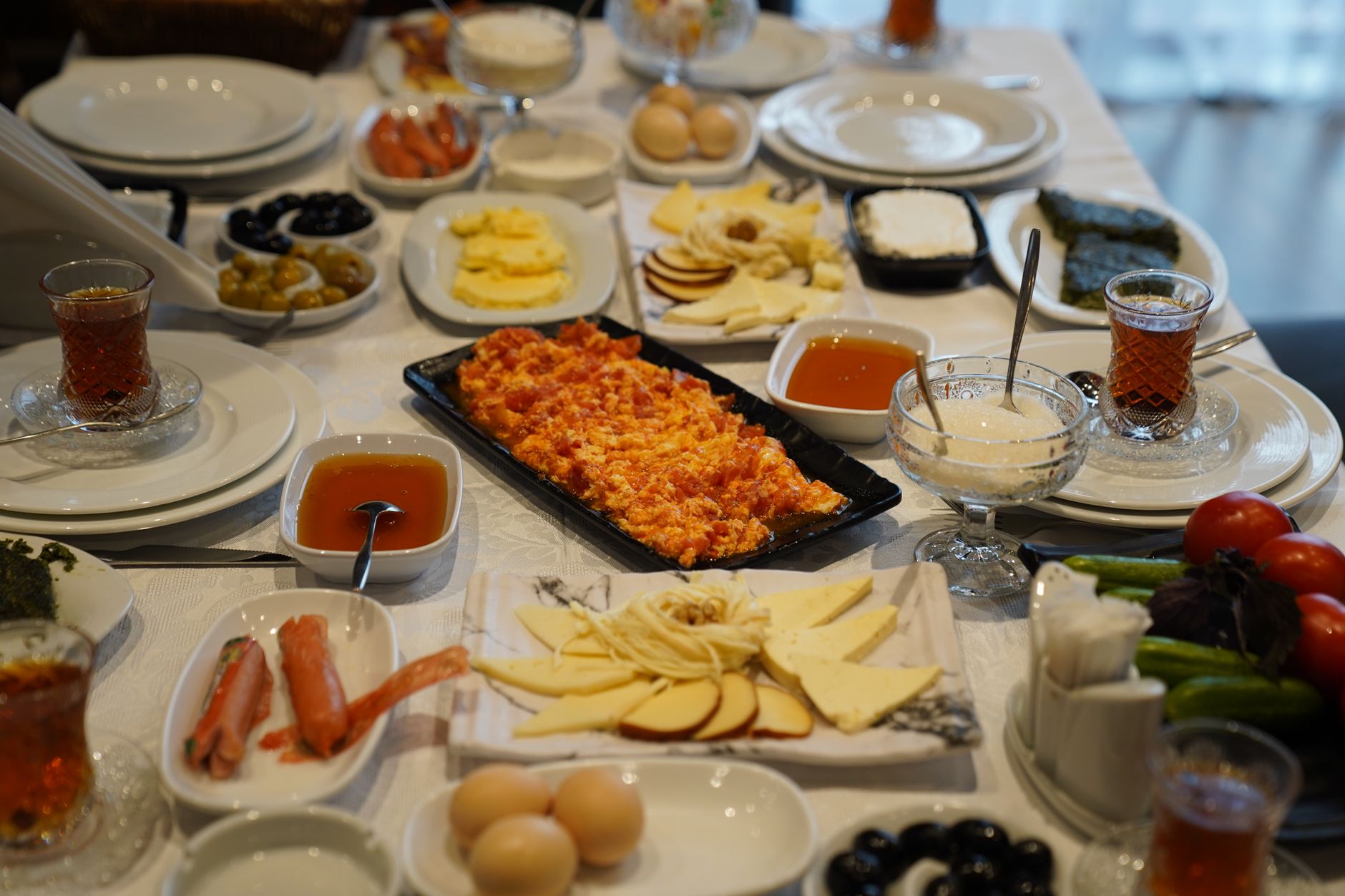 Ein reich gedeckter Frühstückstisch mit verschiedenen Käsesorten, frischem Gemüse, gekochten Eiern und traditionellen Teigwaren