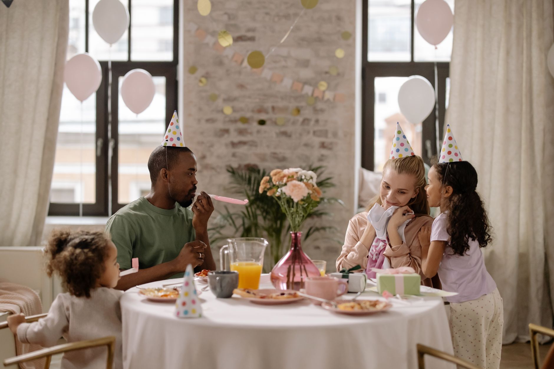 Eine Familie mit Partyhüten sitzt fröhlich an einem reich gedeckten Geburtstagstisch im Kreis ihrer Liebsten
