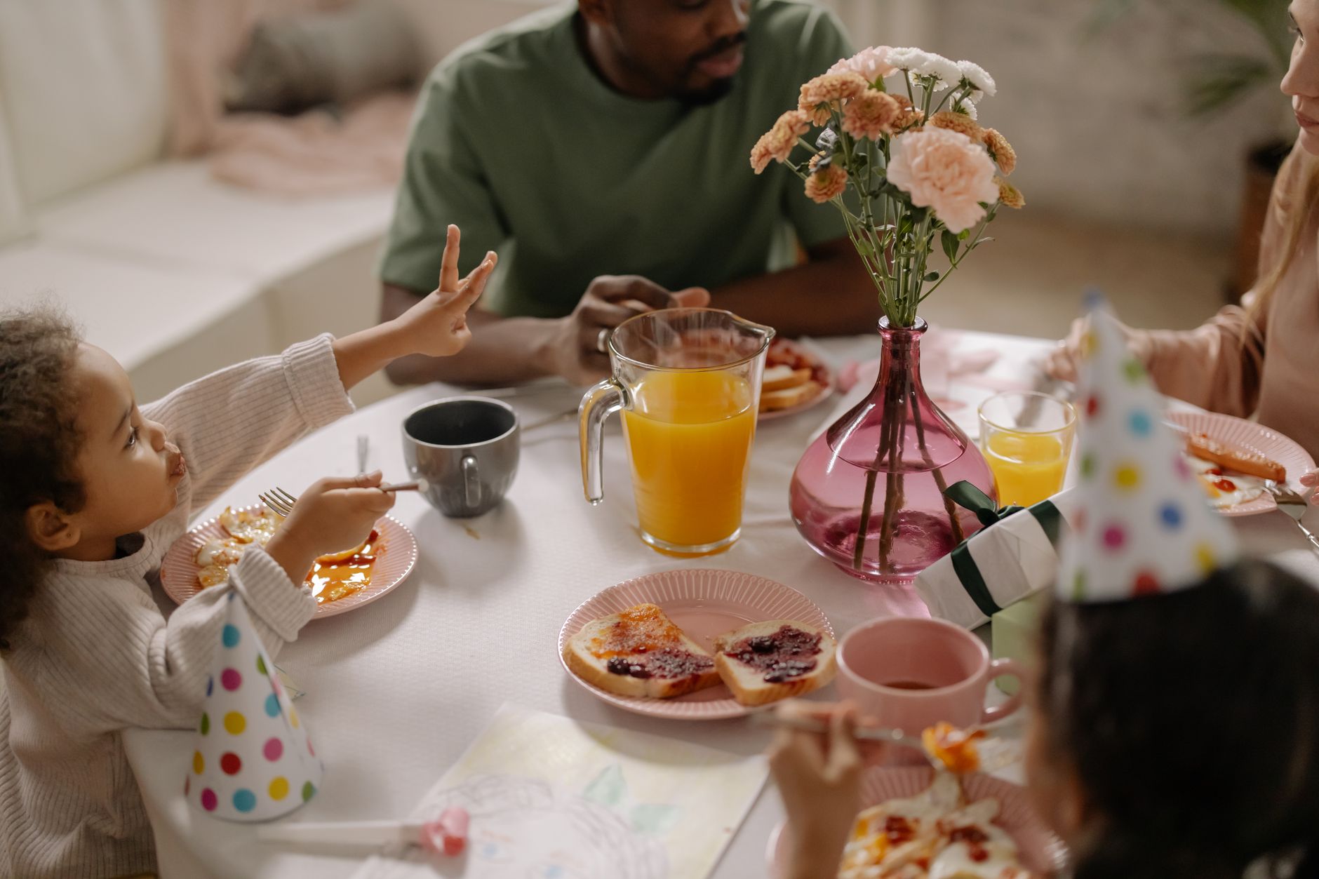 Eine fröhliche Familie sitzt an einem hell gedeckten Frühstückstisch zusammen und feiert gemeinsam mit den Kindern.