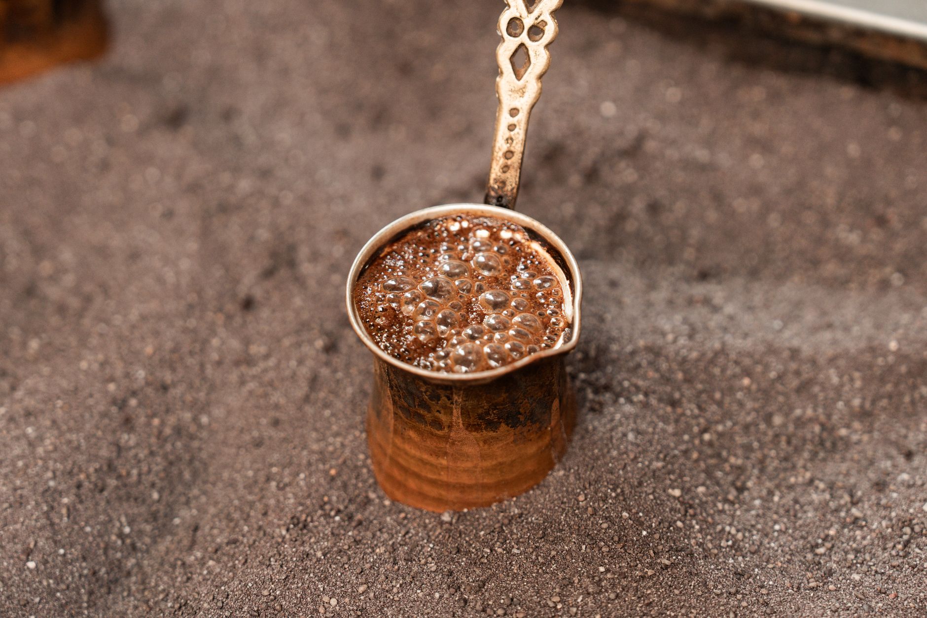 Traditionelle Zubereitung von türkischem Mokka in einem verzierten Kännchen aus Kupfer mit dichtem, goldbraunem Schaum an der Oberfläche