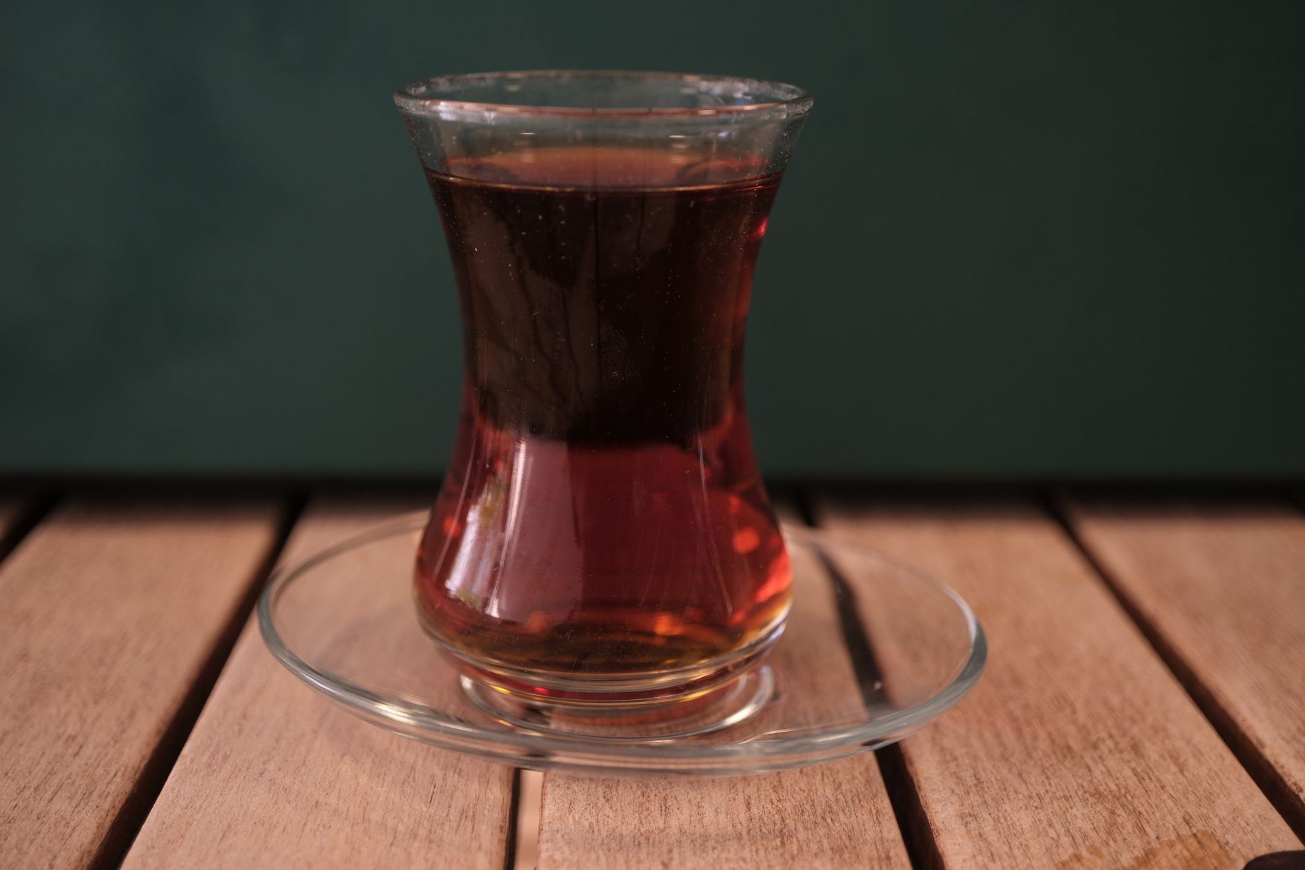 Ein traditionelles türkisches Teeglas in Tulpenform gefüllt mit rötlich-braunem Schwarztee auf einer Untertasse mit einem kleinen Löffel auf einem Holztisch