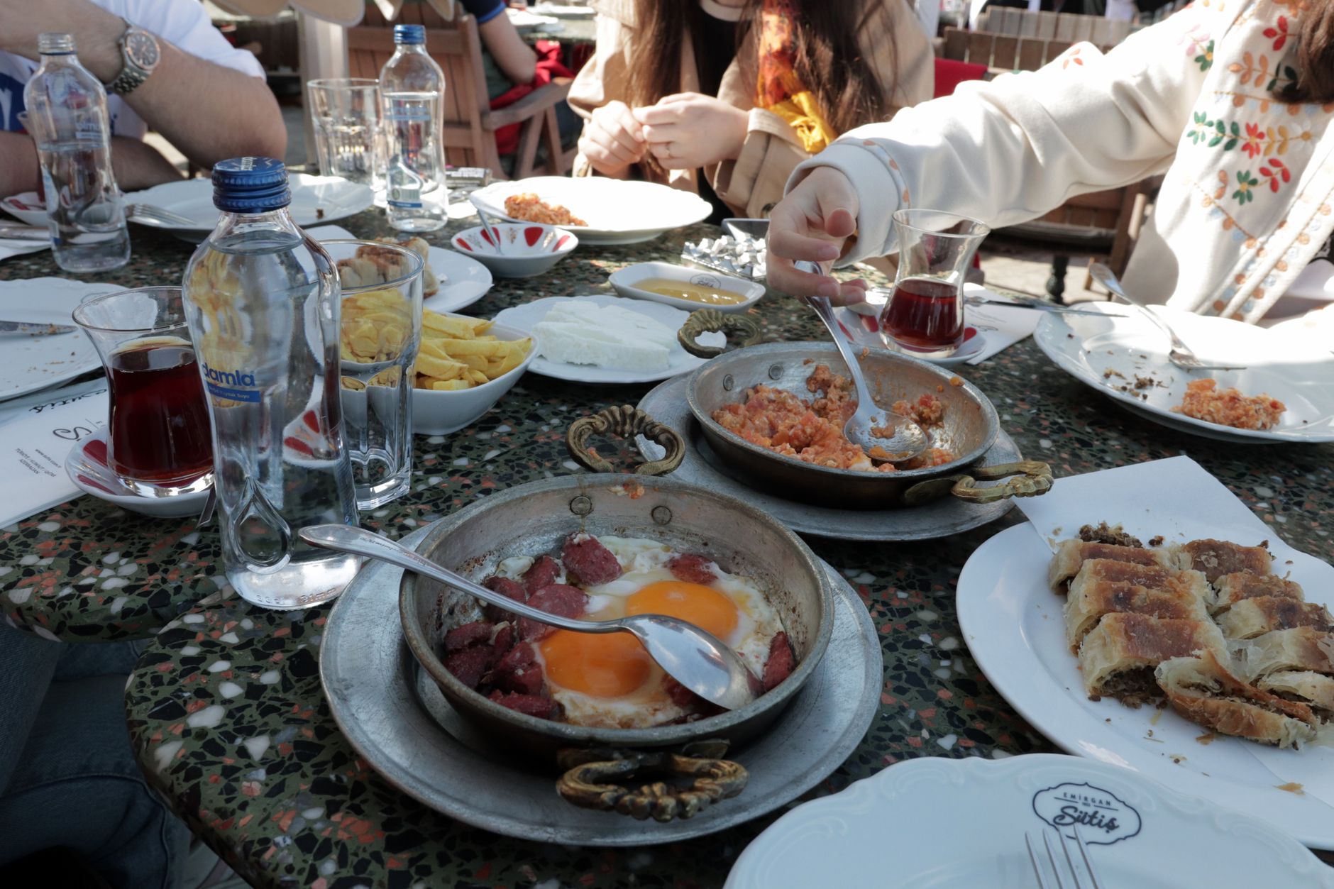 Eine reich gedeckte türkische Frühstückstafel mit vielen kleinen Schälchen, frischem Gemüse, Käse und traditionellen Teegläsern in geselliger Runde.