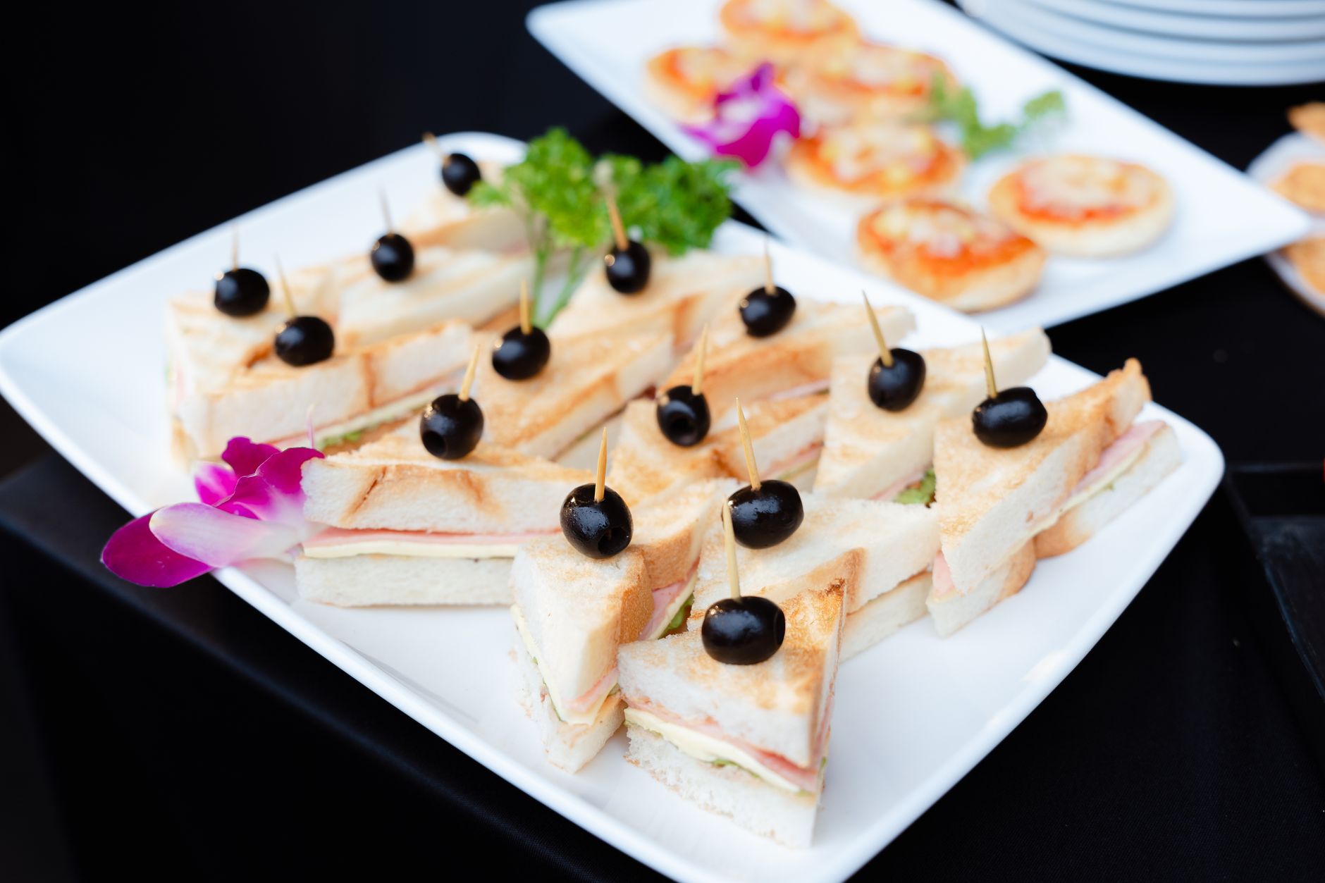 Eine elegante Platte mit mundgerechten Mini-Sandwiches, die mit schwarzen Oliven garniert sind, bereitgestellt für ein Catering-Event.